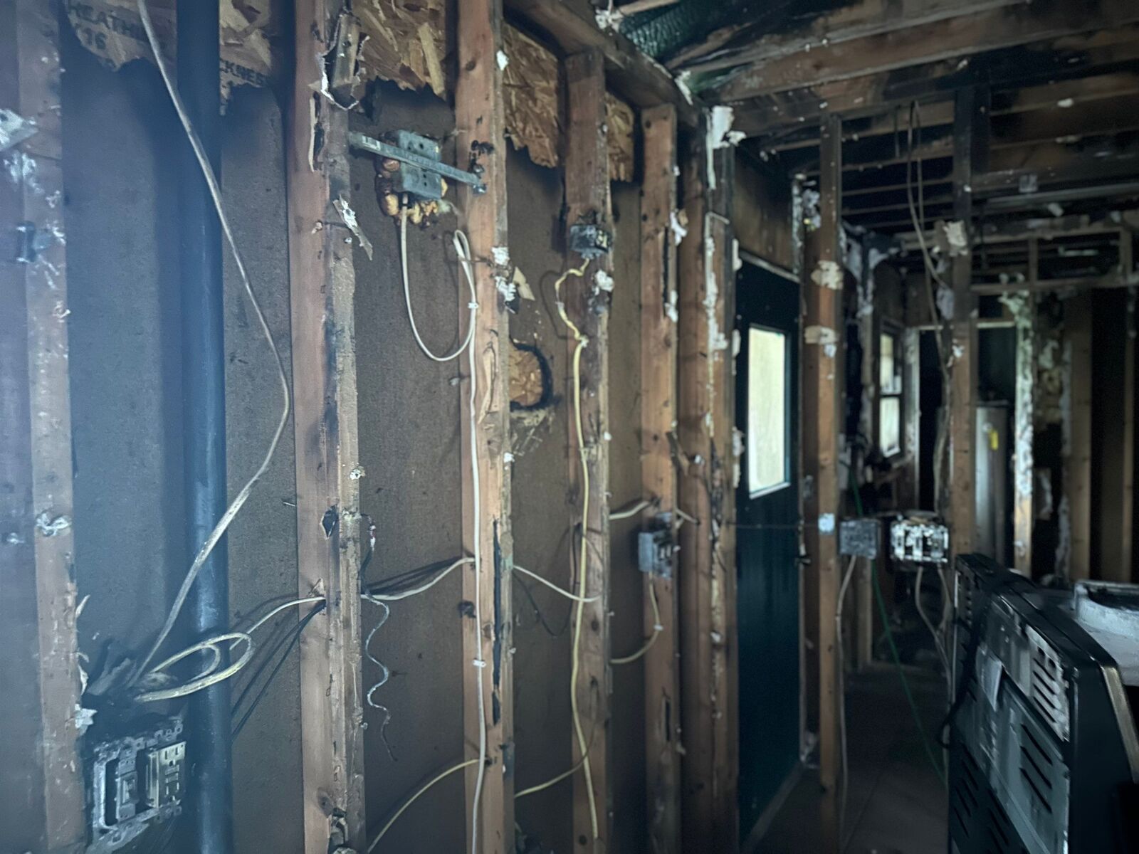 Interior hallway stripped to the studs after a house fire, with burned framing and wiring